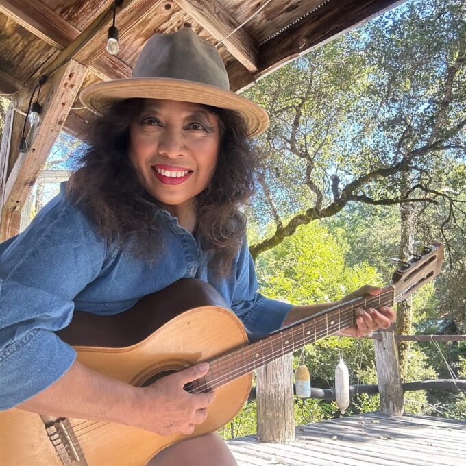 Michellar, Michelle Bond, smiling with an acoustic guitar on a wooden porch