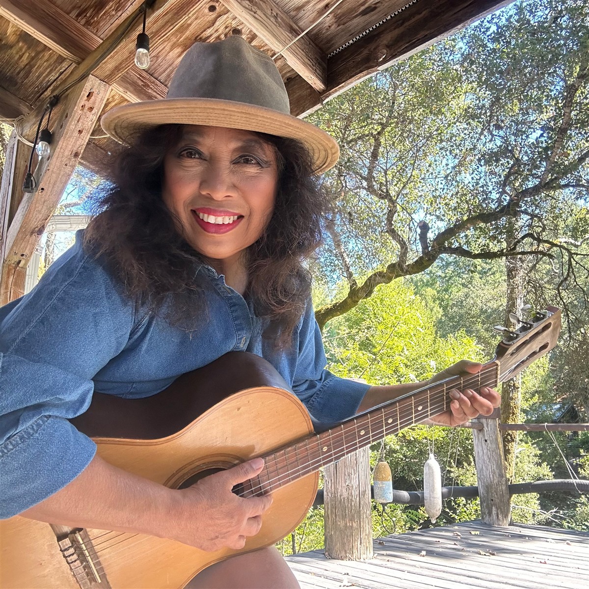 Michellar, Michelle Bond, smiling with an acoustic guitar on a wooden porch